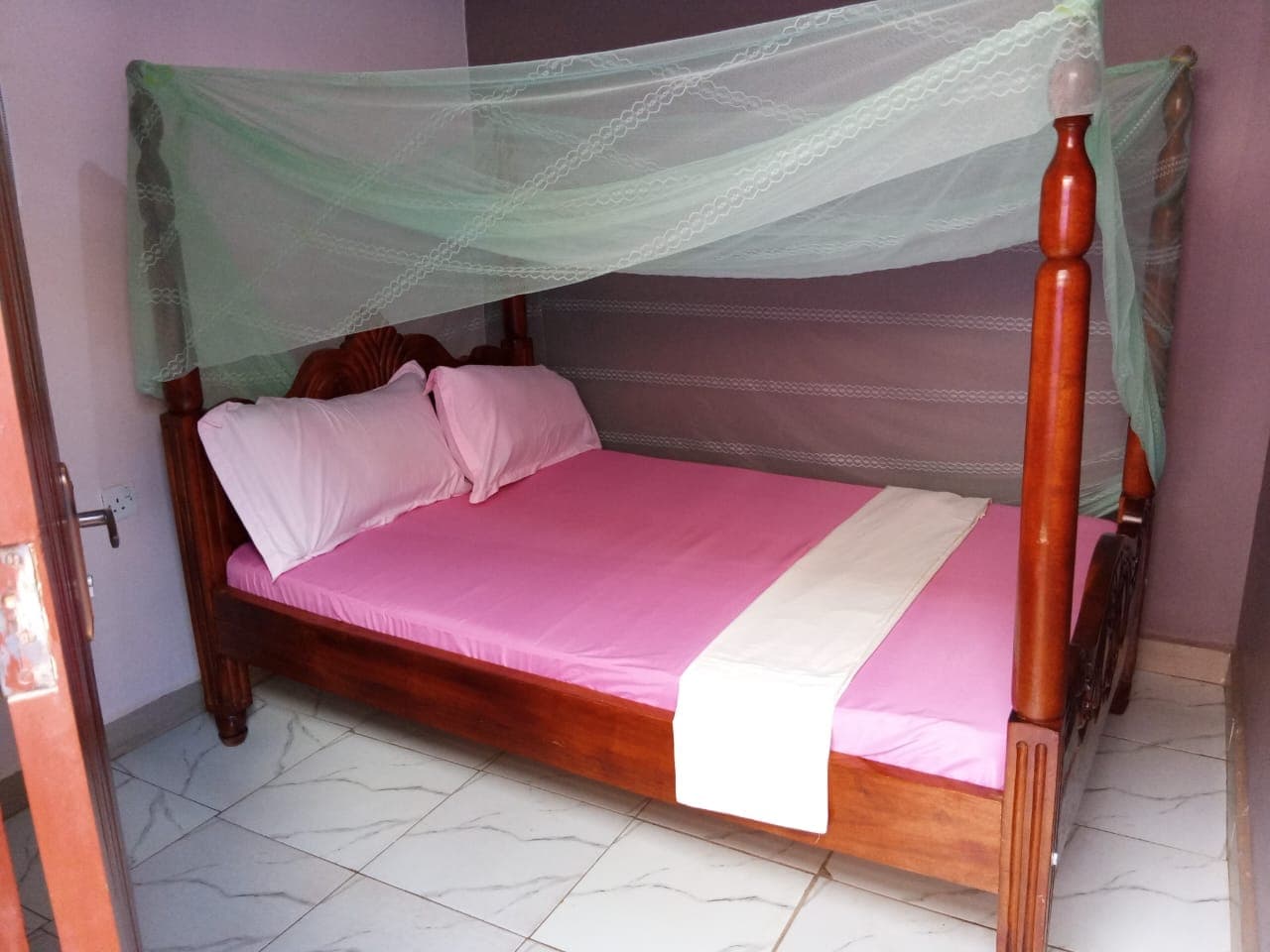 Bright double room with a wooden bed, mosquito net and fresh linen at Eden's Guest House