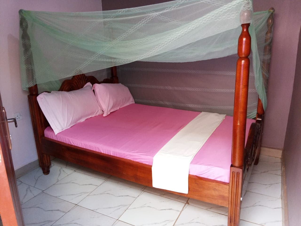 Self-contained double room with a neatly made bed and mosquito net