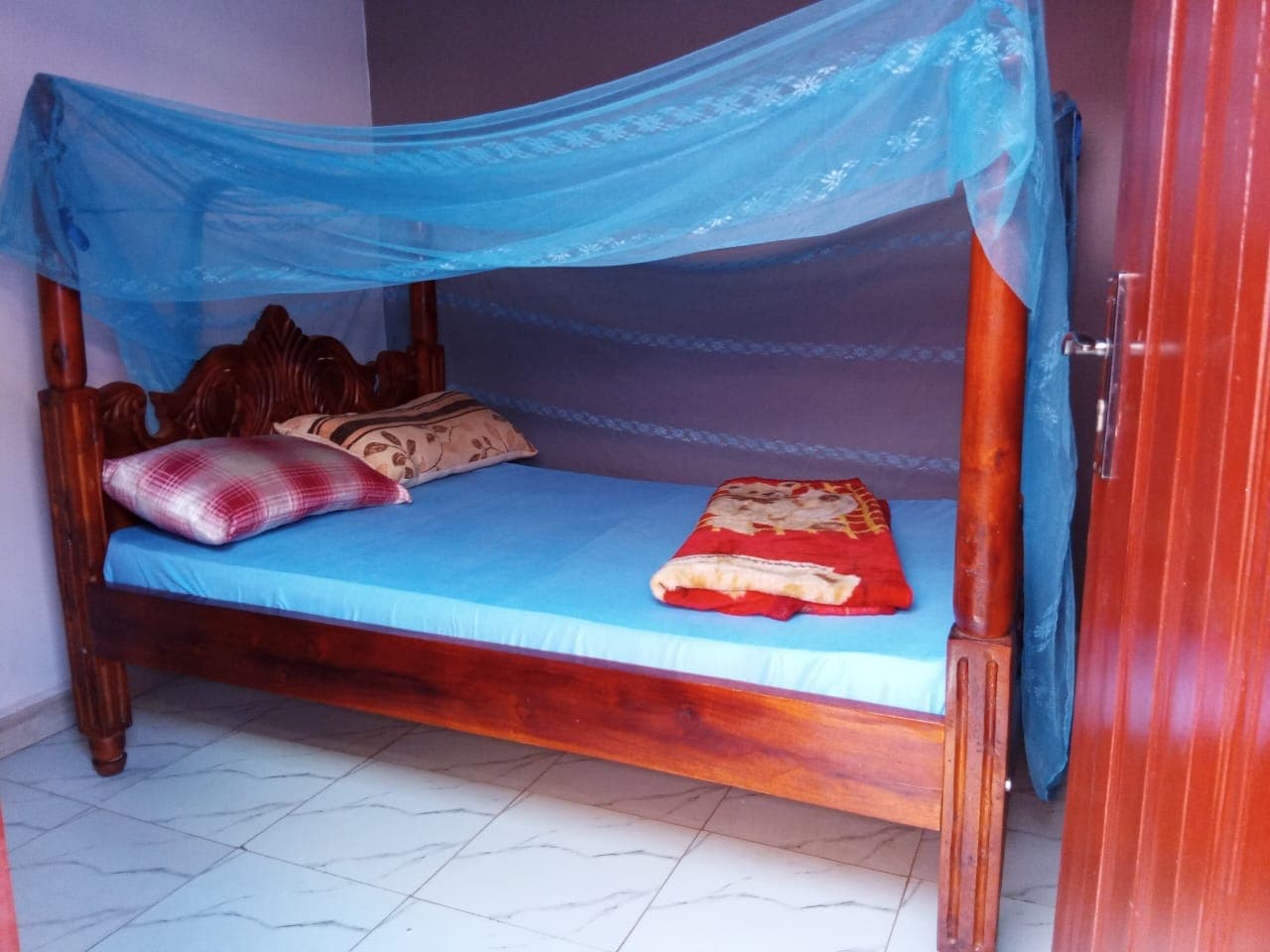 Standard double room with a cosy bed, cushions and a blue mosquito net